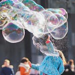 A child delights in chasing and popping giant bubbles in an outdoor setting.